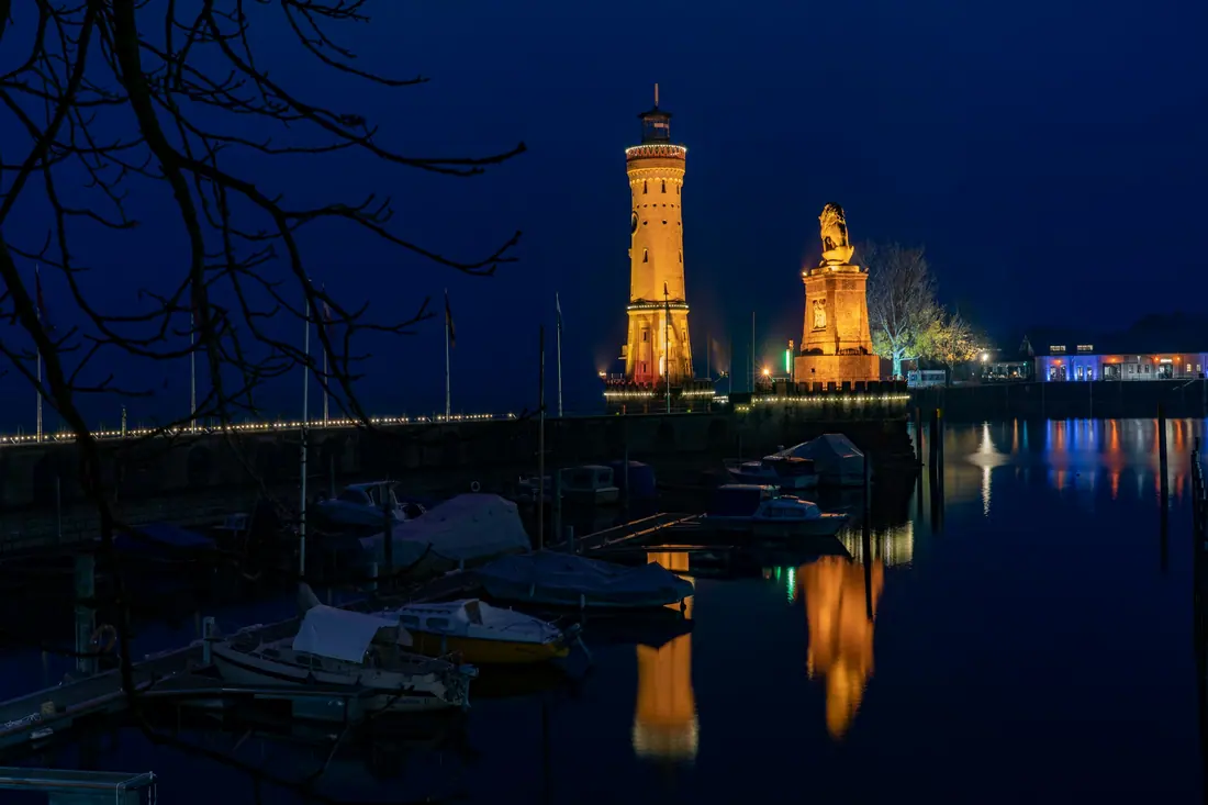 Lindau harbour at night, with the lit lighthouse and the lion monument reflected in the water