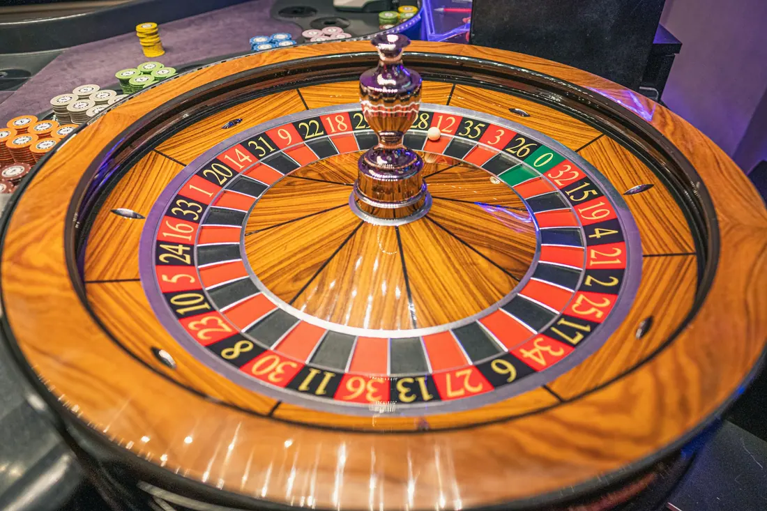 A roulette wheel photographed close up, with its numbered pockets and a stack of chips at the edge of the table