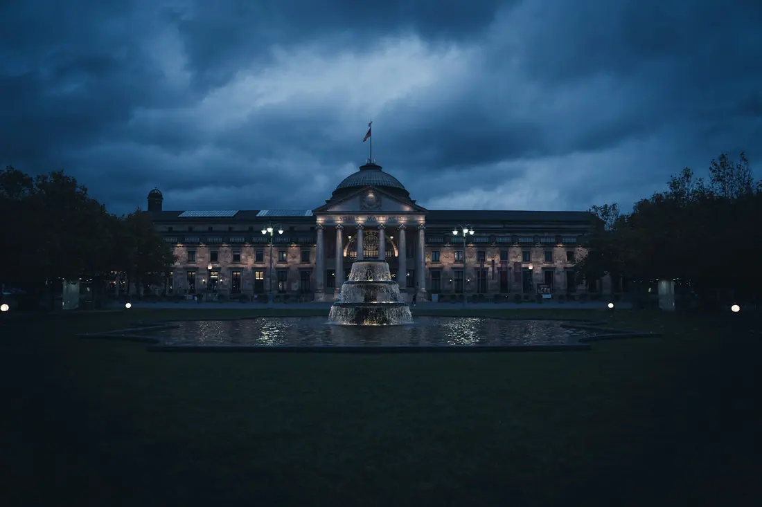 The domed Kurhaus in Wiesbaden under a dark evening sky, lit across a still lawn